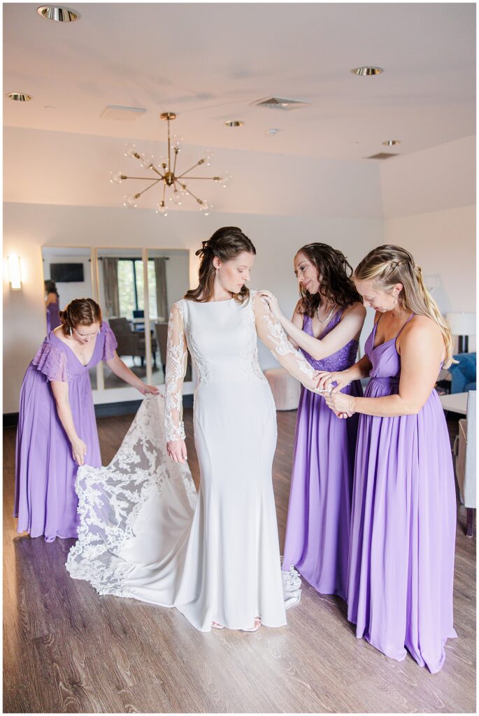 Bridesmaids helping bride into dress 