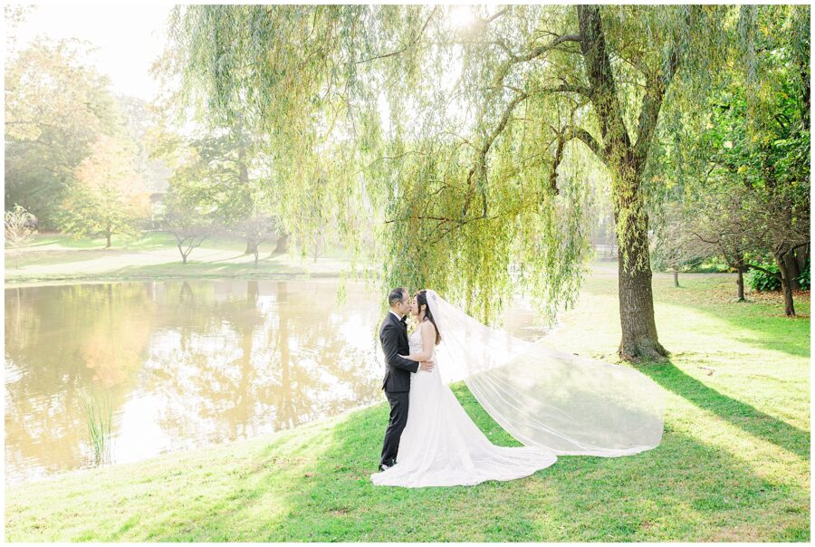 Bride and groom kissing with wedding veil blowing in the breeze