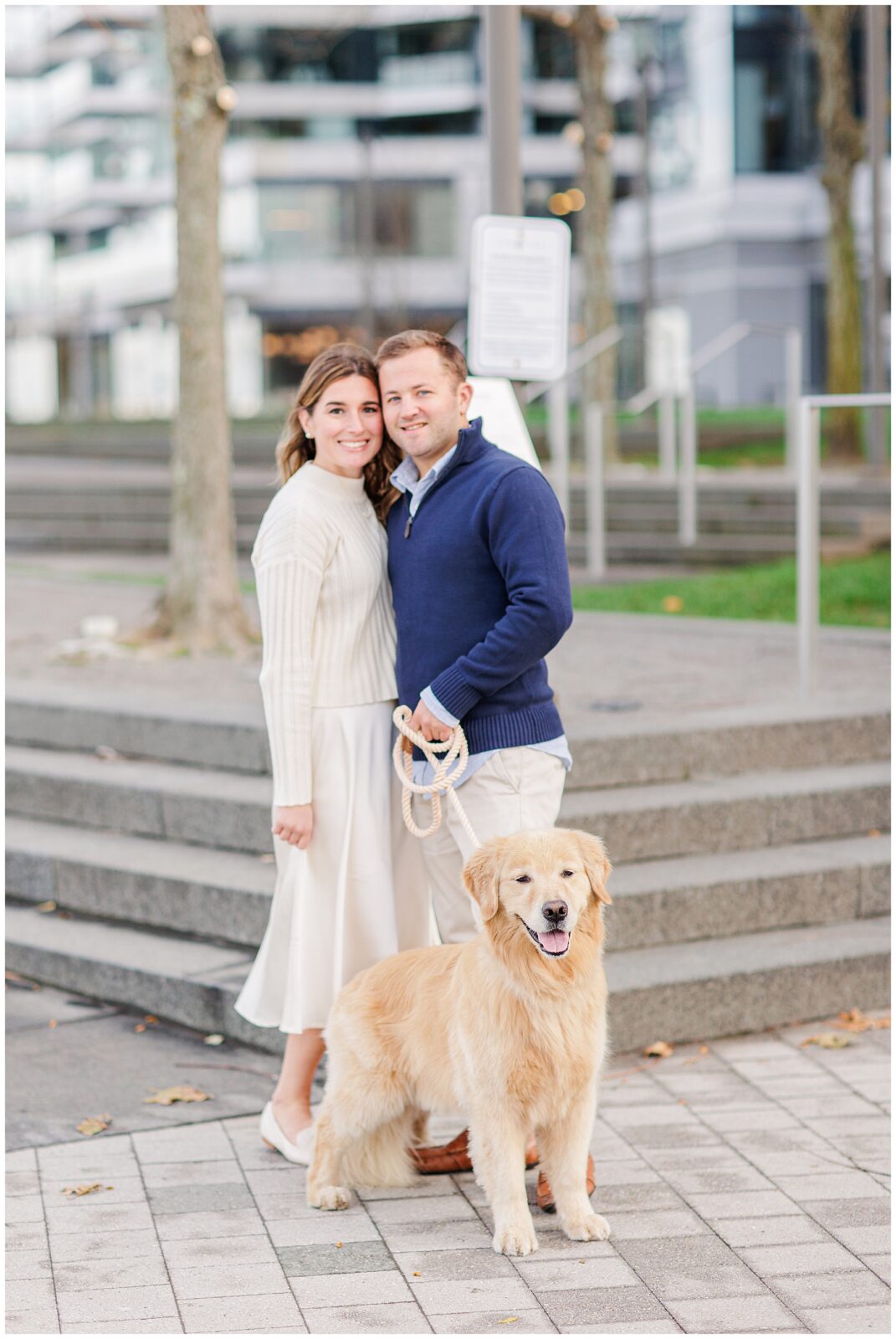 Couple is hugging while also holding the leash for their golden retriever.