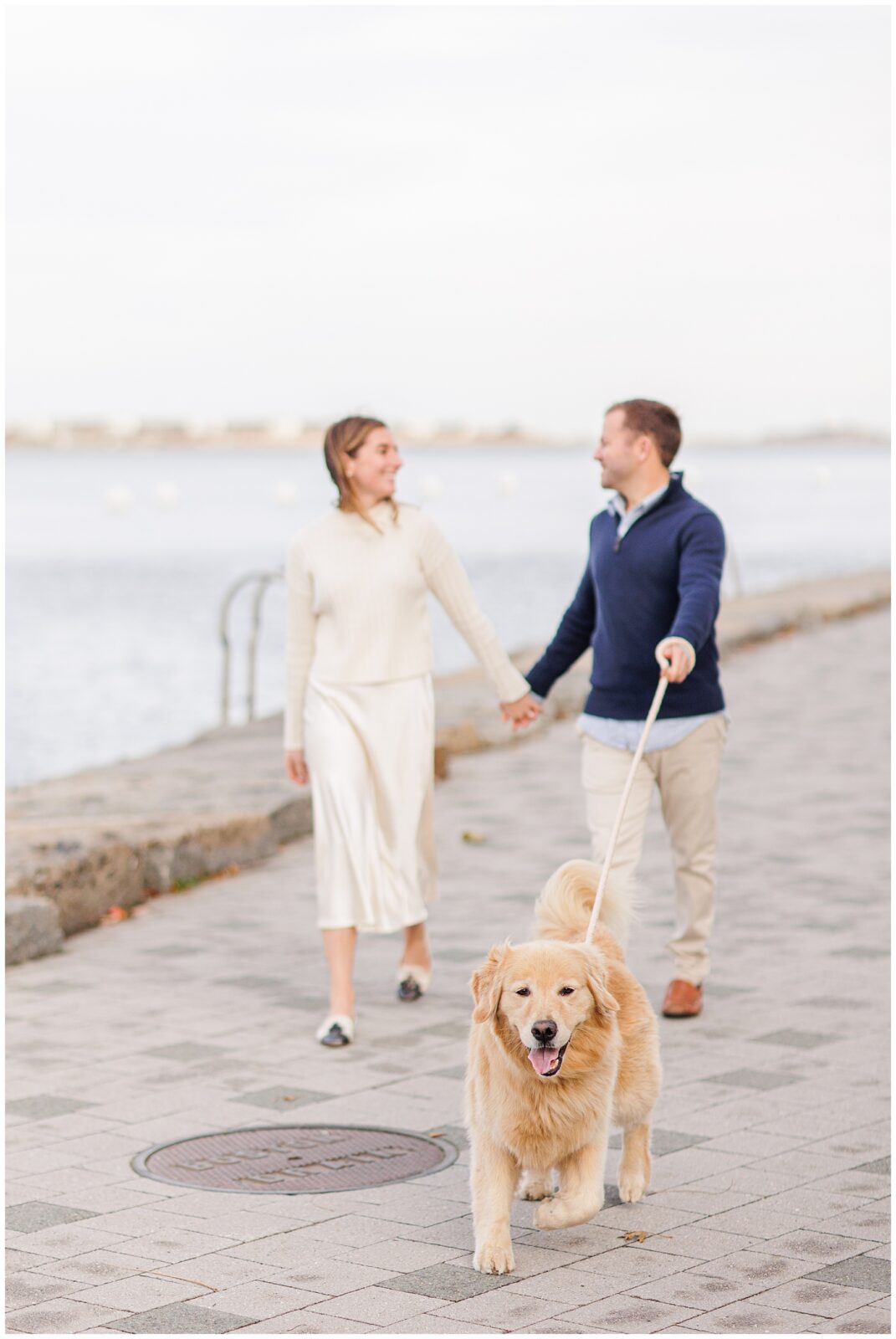 Couple holding hands while walking their dog during Boston Seaport engagement session.