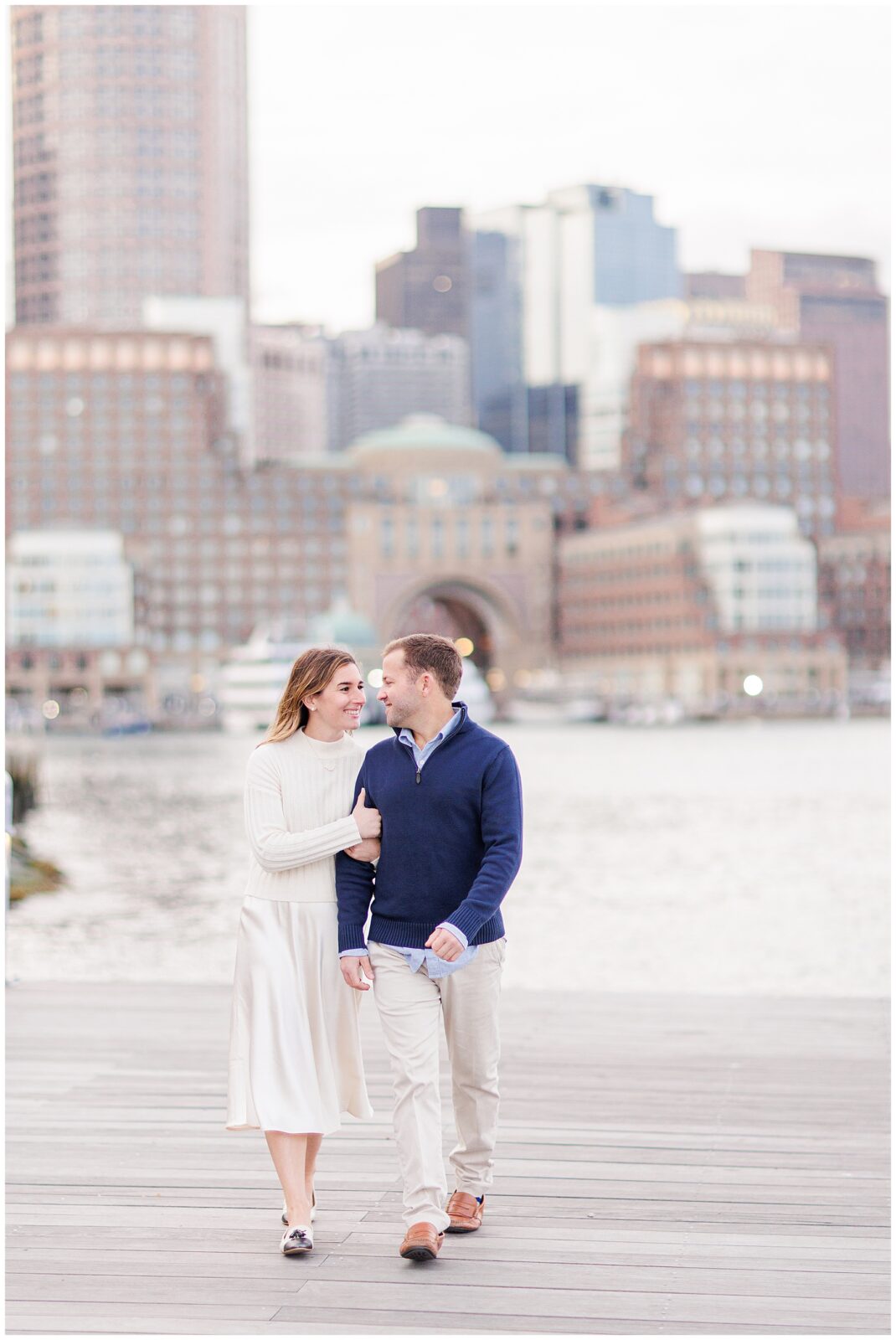 Man and woman walking during their Boston Seaport engagement session.