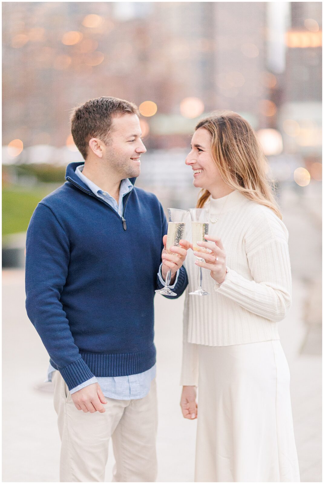 Couple clinking champagne glasses during Boston Seaport engagement session. 