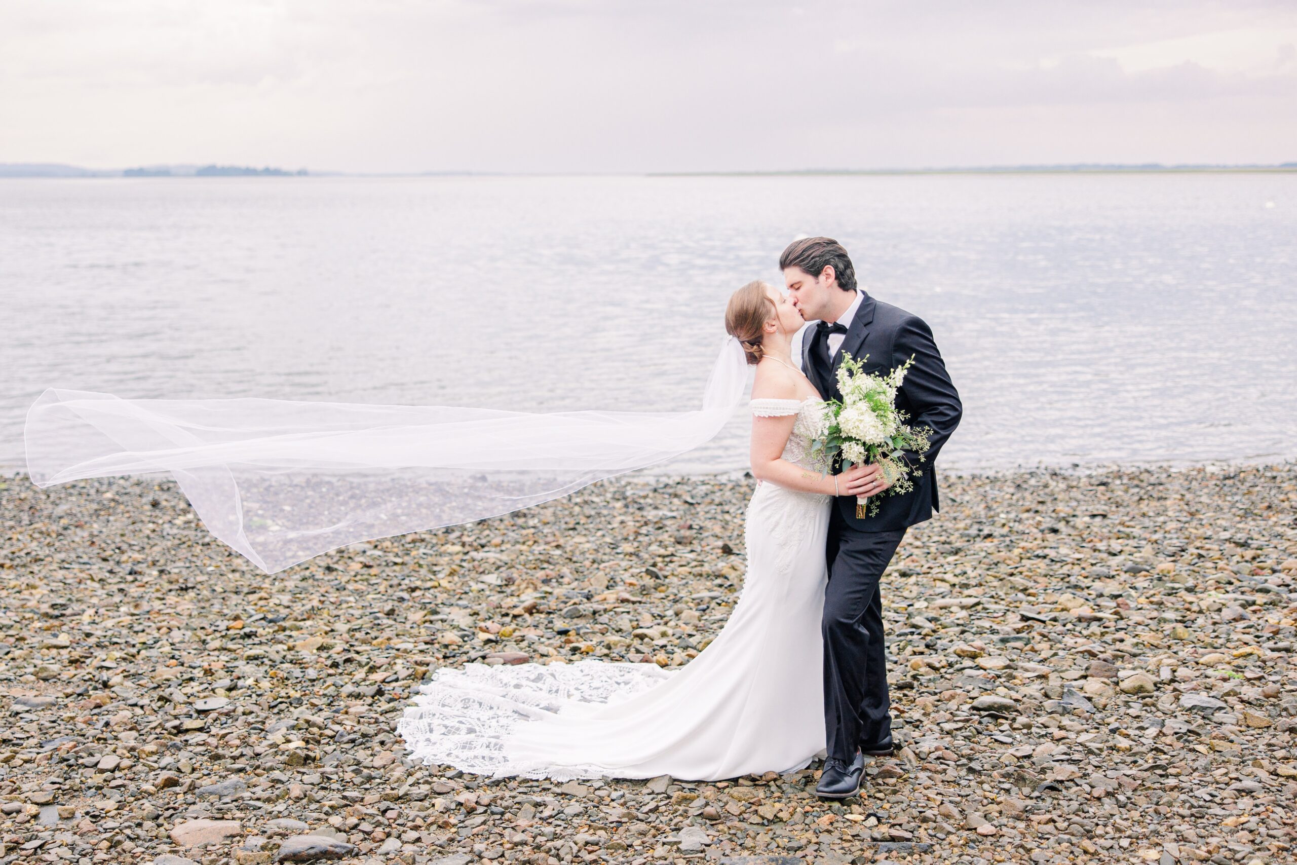 Bride and groom on the beach with veil flowing behind the bride