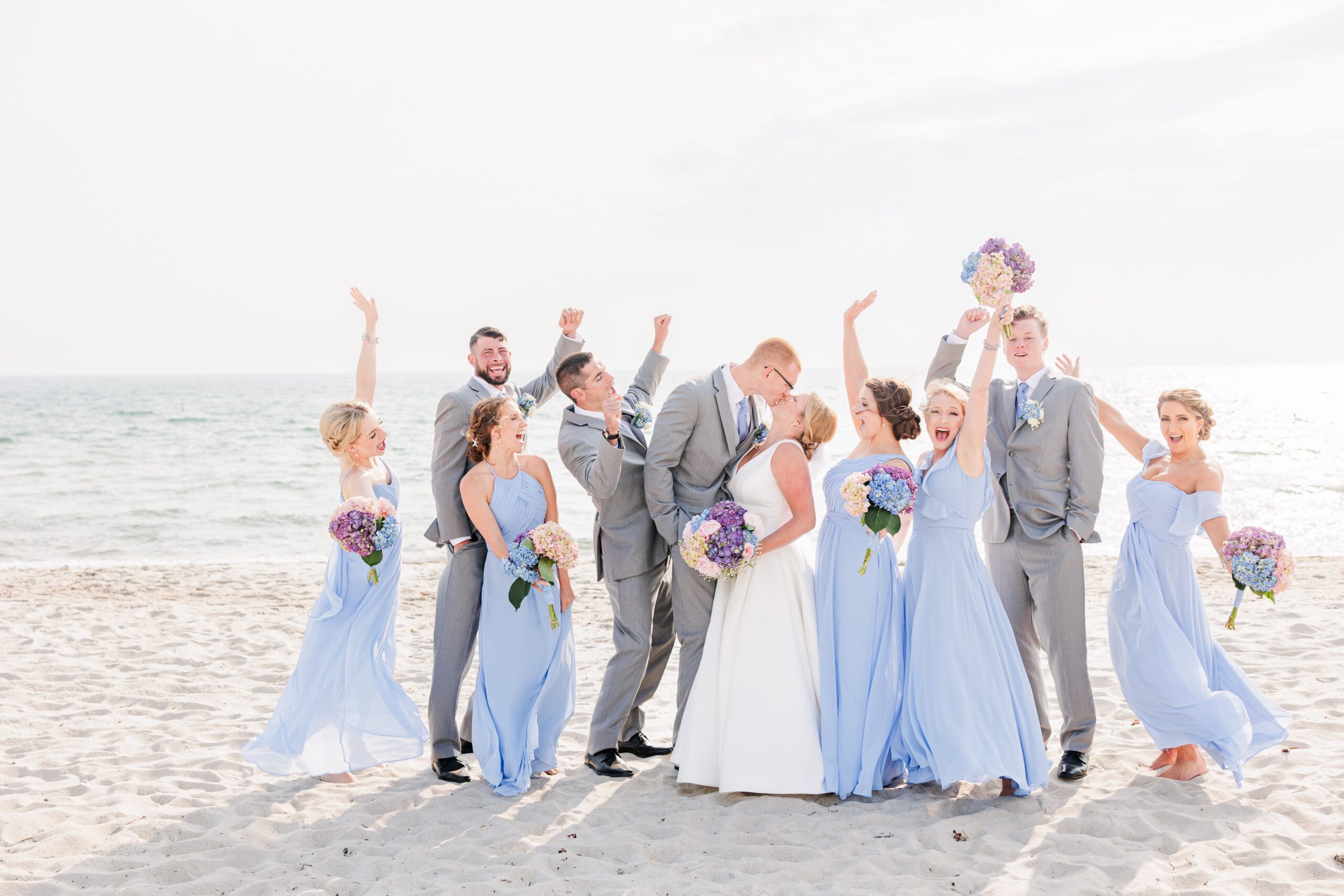 Wedding party cheering while bride and groom kiss on the beach