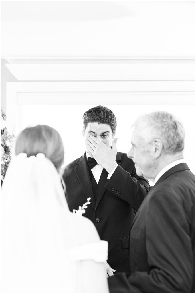 Groom wiping away tear when he sees bride coming down the aisle