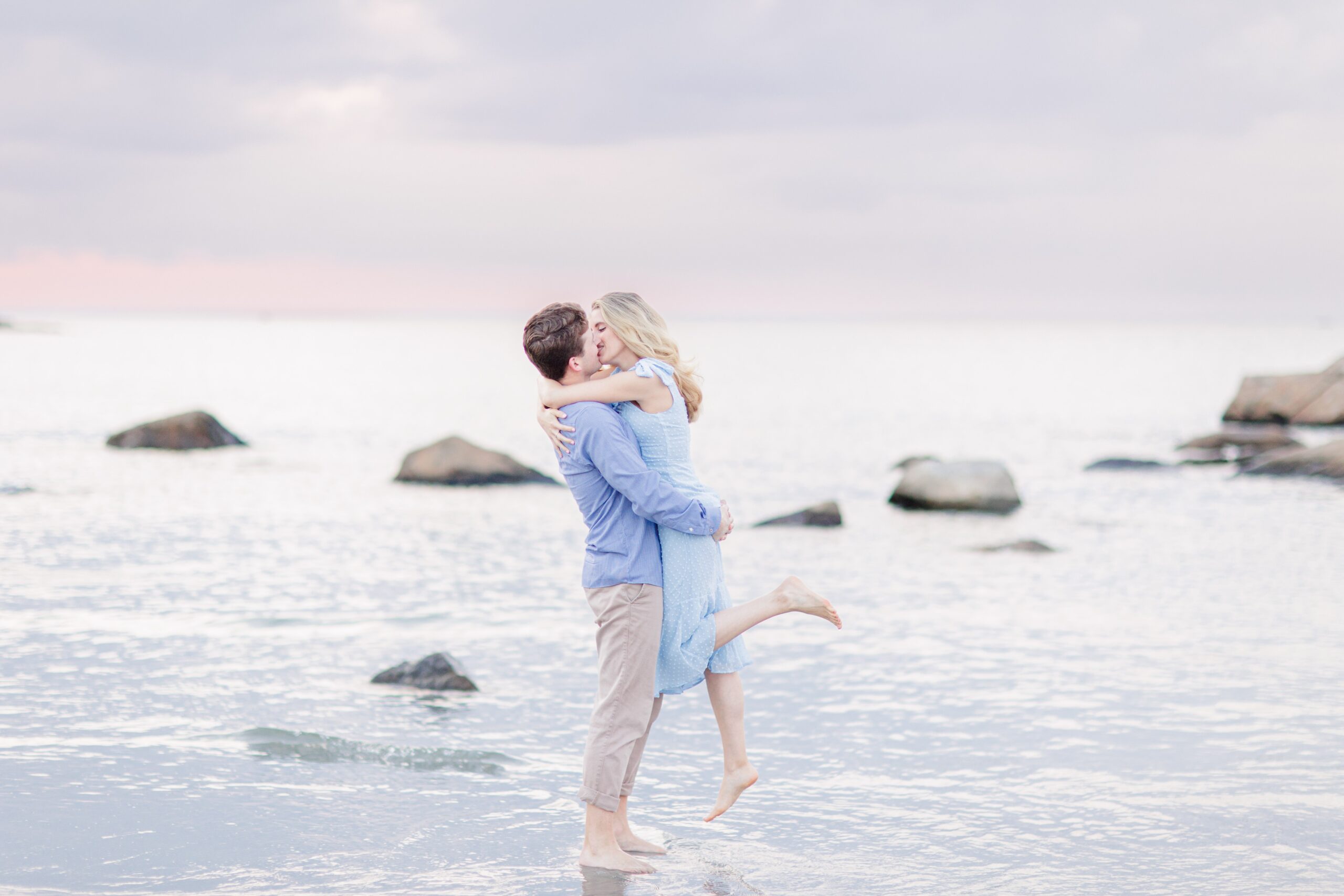 Man holding and kissing a woman at the beach in front of the sunset