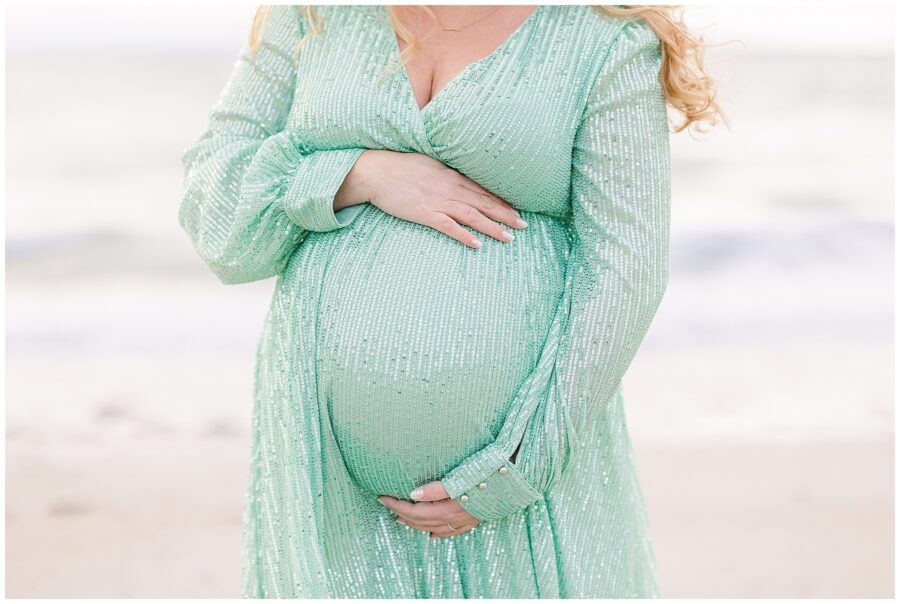 Close up of a woman wearing a sequined green dress holding her baby bump