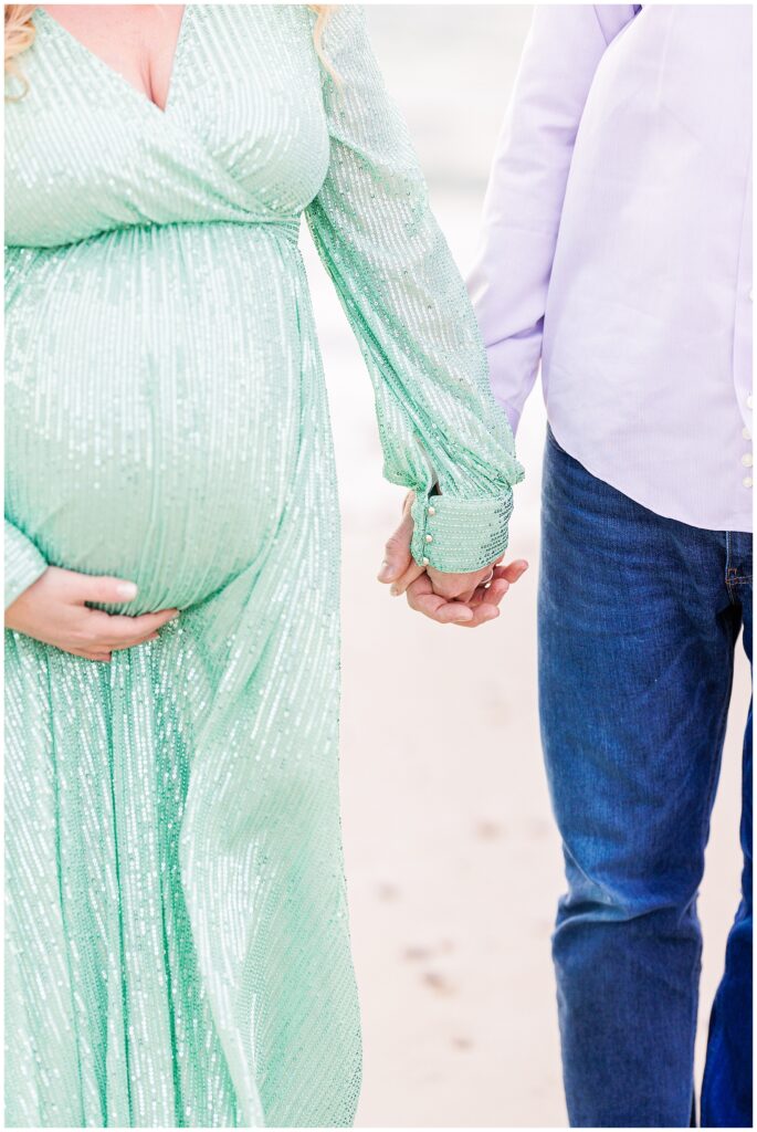 Couple holding hands while the woman holds her baby bump