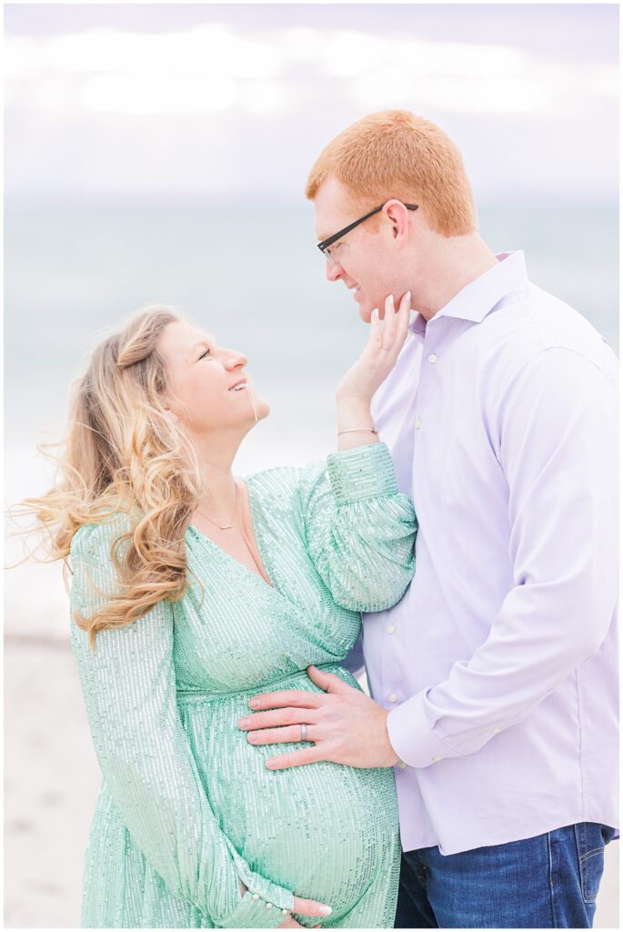 Woman smiling at her husband and touching his face while he touches her baby bump