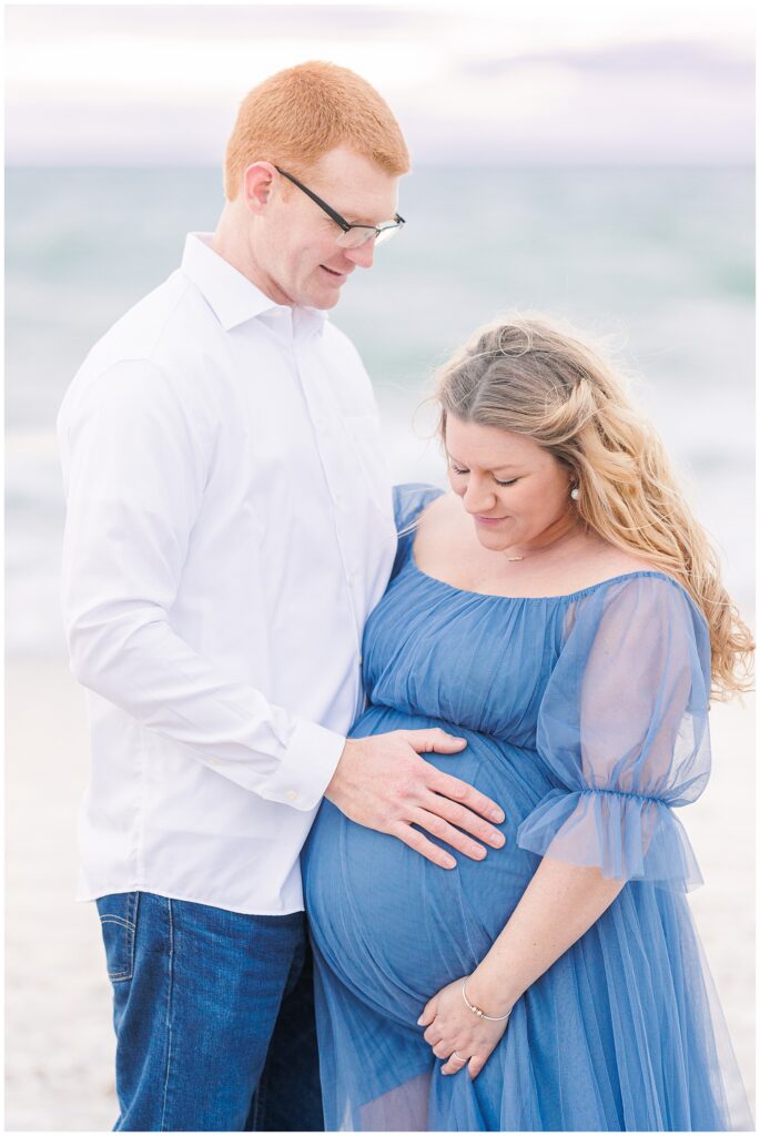 Man and woman holding baby bump and looking down at baby bump Cape Cod maternity pictures