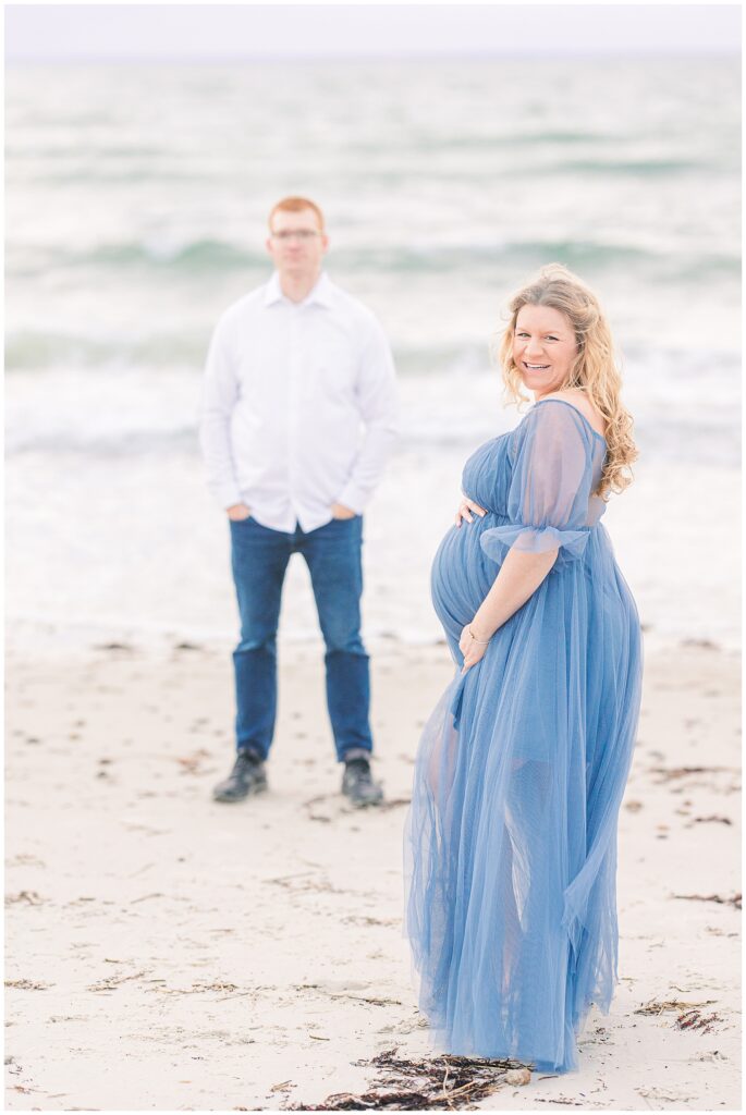 Woman holding her baby bump and looking at the camera while her husband stands in the background