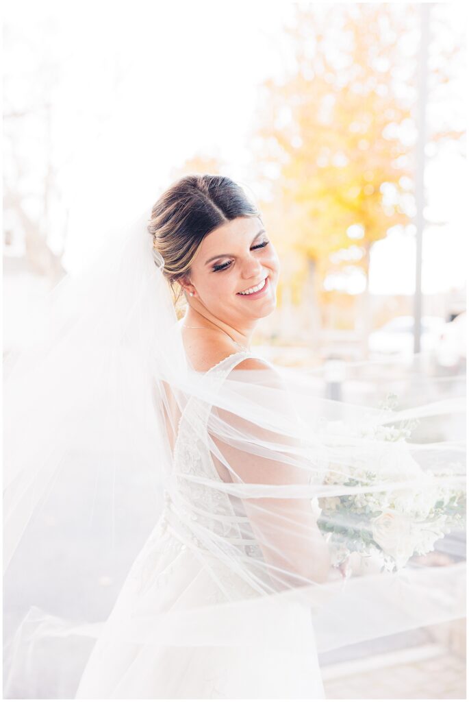 Bride laughing over her shoulder as her wedding veil blows in the breeze