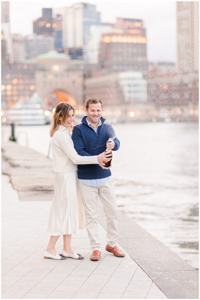 Couple popping a champagne bottle at Fan Pier Park in Boston during their engagement photos