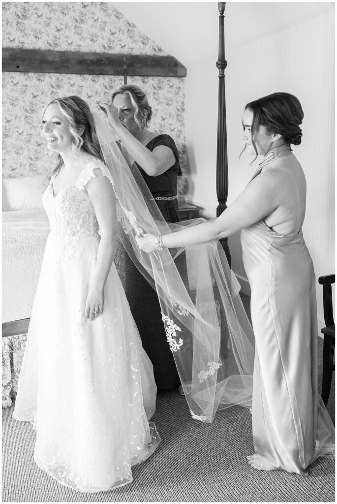 Maid of honor and mother of the bride putting a veil on the bride