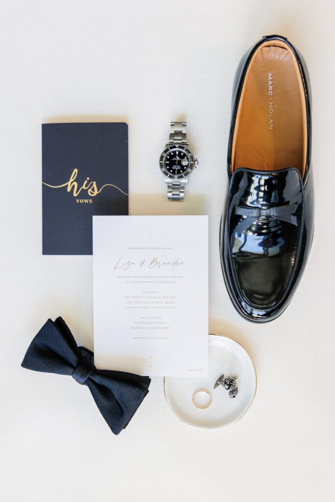 Groom wedding detail pictures flatly including shoes, a vow book, a watch, the wedding invitation, a bow tie, a wedding band, and cuff links