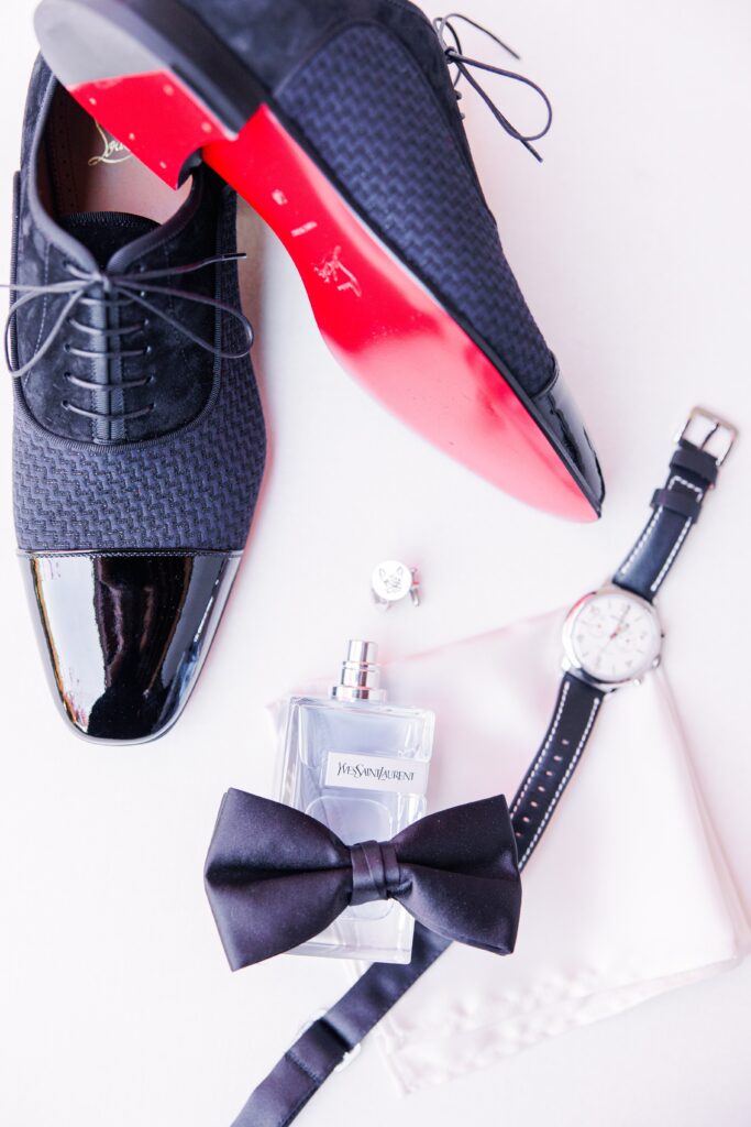 Groom details including shoes, a watch, cuff links, cologne, a bow tie, and a pocket square representing wedding detail pictures