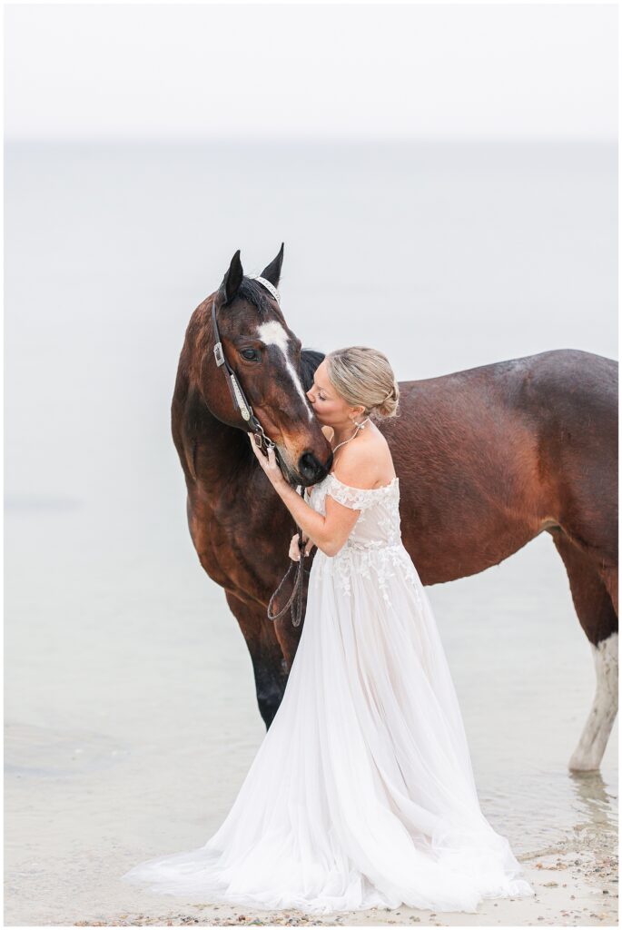 Bride standing in the ocean and kissing her horse during her Cape Cod Bridal portrait session