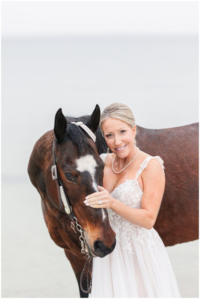 Bride petting her horse's nose at Old Silver Beach in Falmouth, MA during her Cape Cod bridal pictures