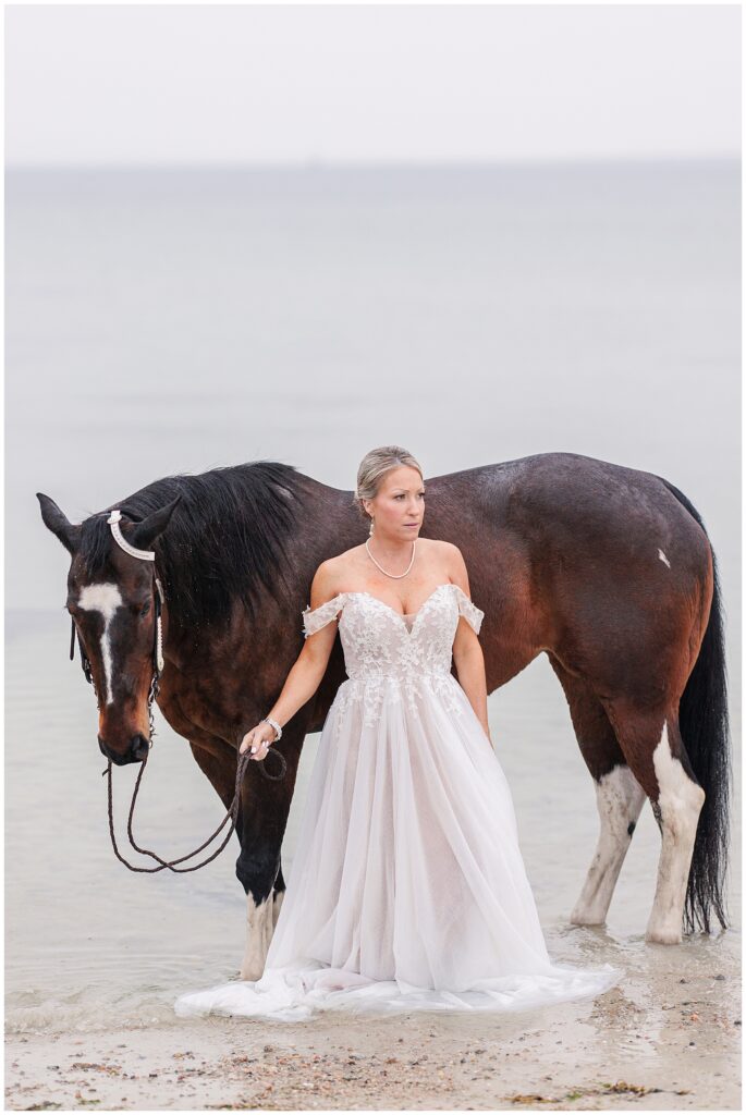 Bride and her horse standing in the ocean waves at Old Silver Beach in Falmouth, MA Cape Cod
