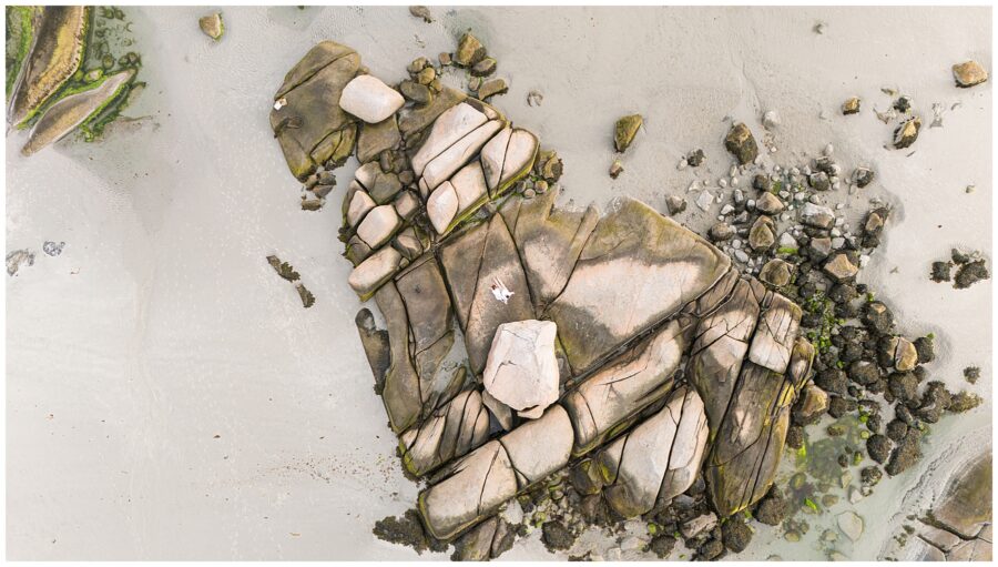 An aerial view of couple sitting on rocks at a Gloucester beach