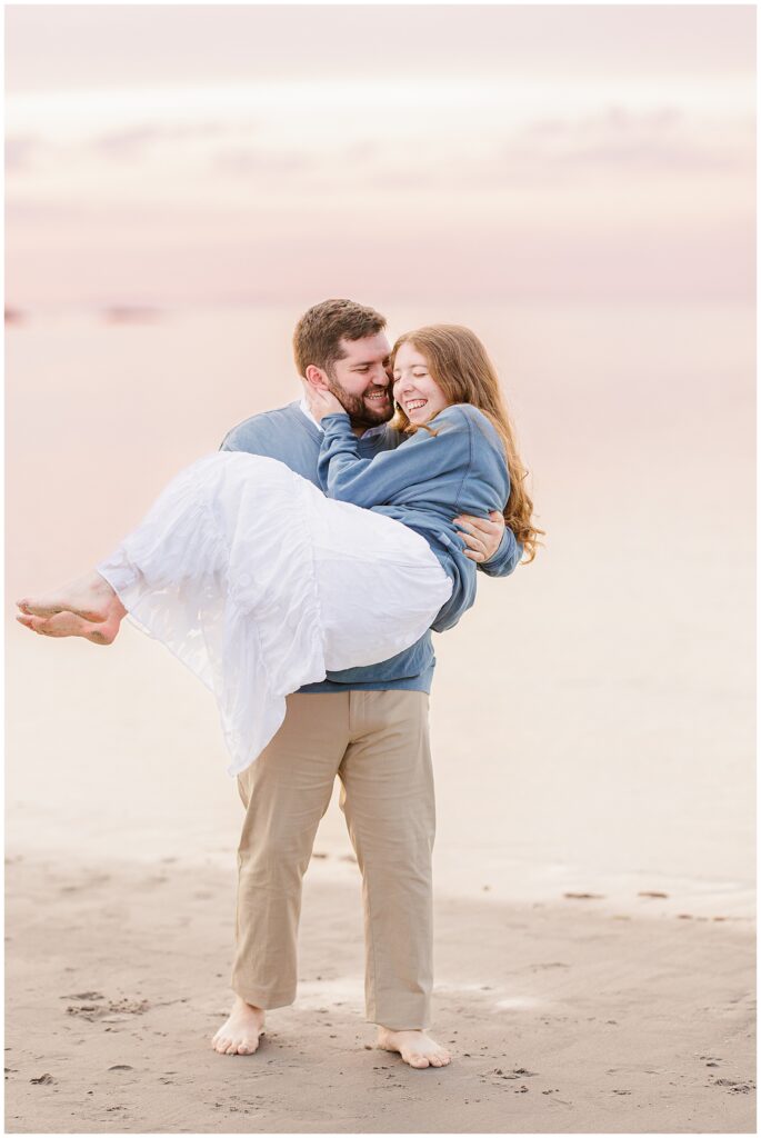 A man picking up a woman and laughing at Wingaersheek Beach