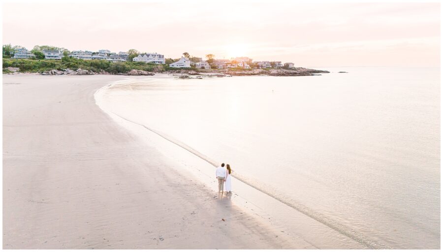 A drone picture of a couple holding hands watching the sunset on a Gloucester beach