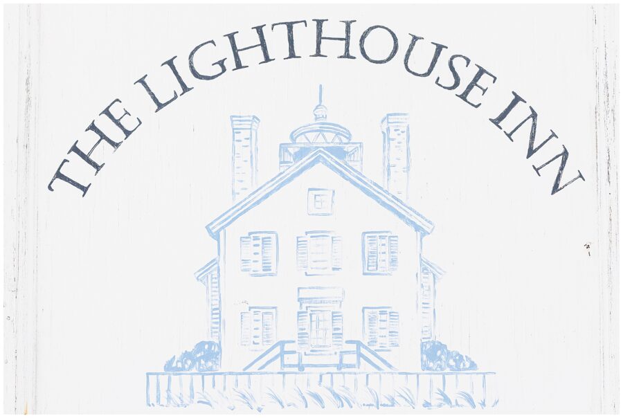 A wooden sign reading “The Lighthouse Inn” with an illustration of a house with a lighthouse on top.