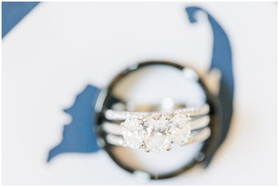 Close-up of a set of three diamond rings, with the engagement ring featuring three large diamonds in the center. The rings are placed on a blue and white background.