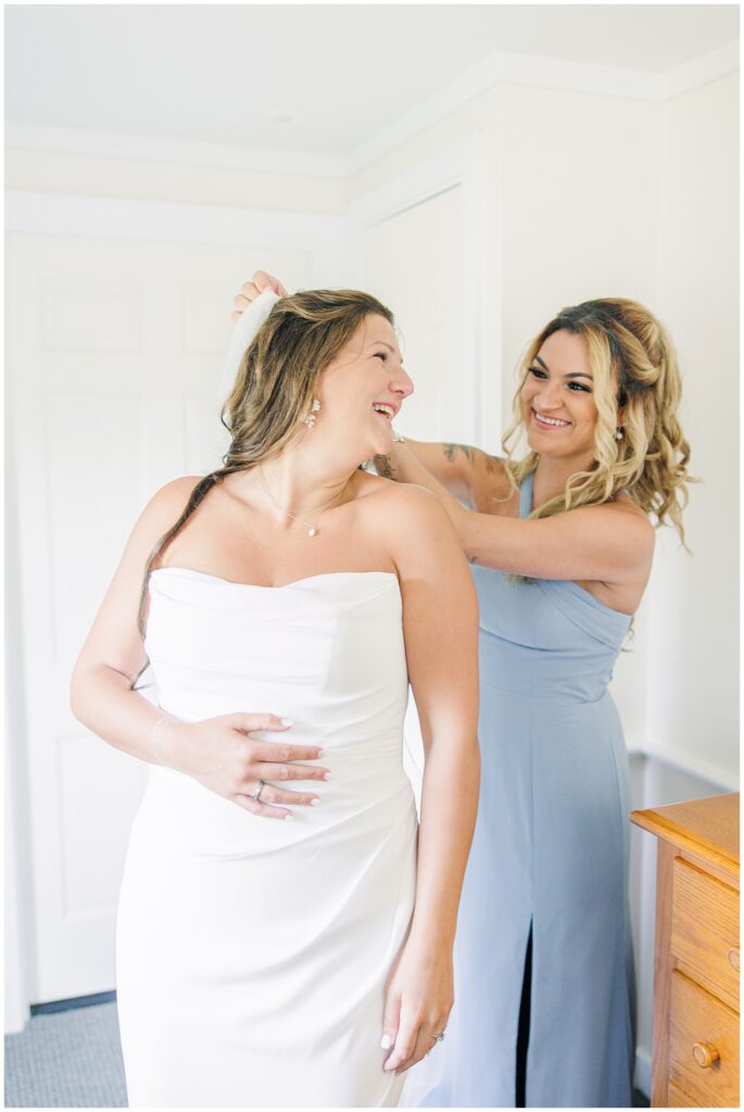 The bride and bridesmaid laughing as the bridesmaid adjusts the bride’s veil.