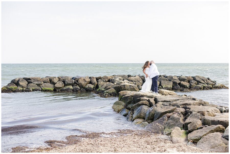 A bride and groom standing on a rocky jetty, kissing with the ocean surrounding them. Location: Lighthouse Inn, Cape Cod.