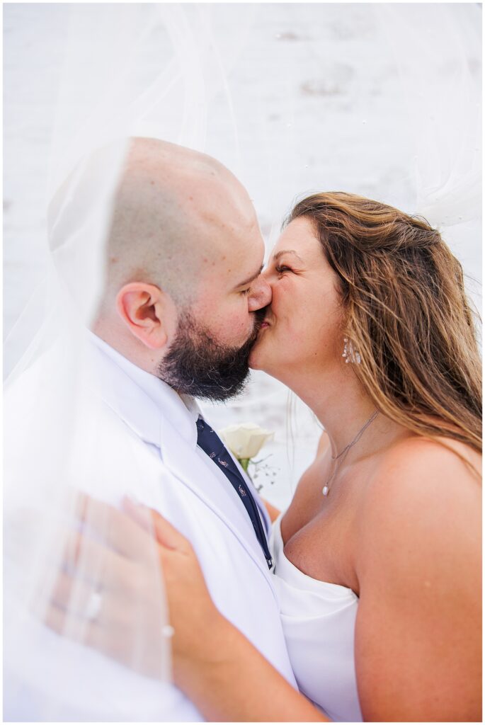 Close-up of a bride and groom kissing, with the bride’s veil flowing around them.