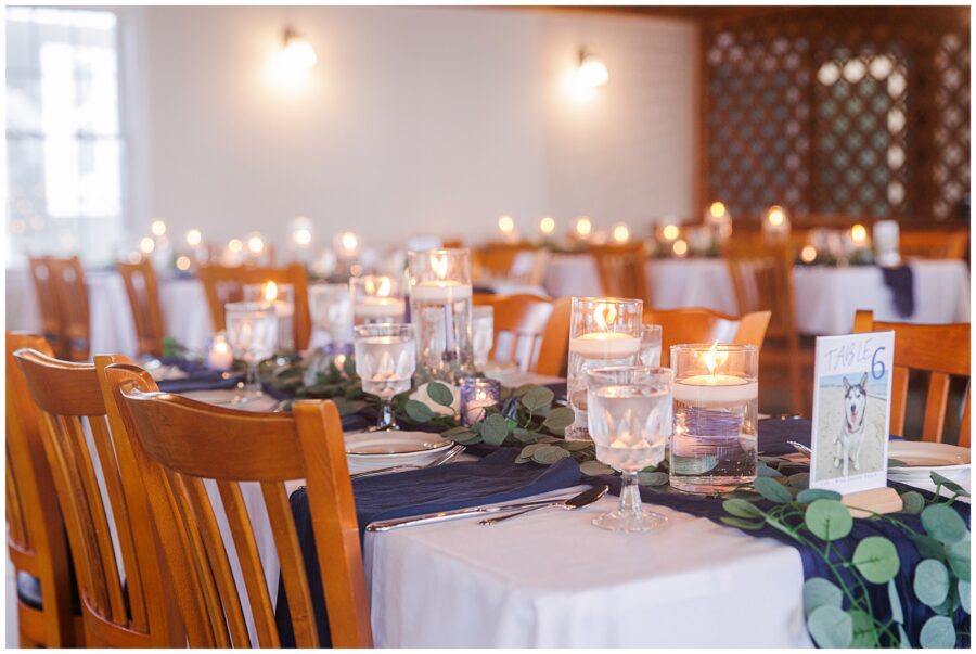 A reception table setting with wooden chairs, white tablecloths, blue napkins, and candle centerpieces. Location: Lighthouse Inn, Cape Cod.