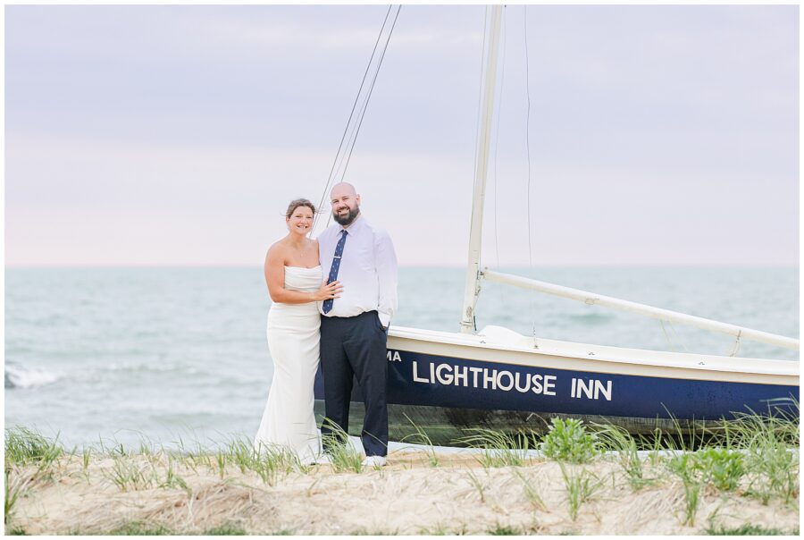 Bride and groom posing by a sailboat with the text “Lighthouse Inn” on the side. Location: Lighthouse Inn, Cape Cod.