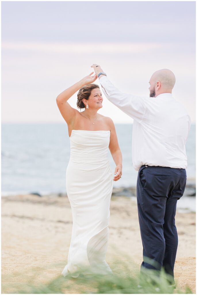 Bride and groom dancing on the beach at sunset, with the groom twirling the bride.