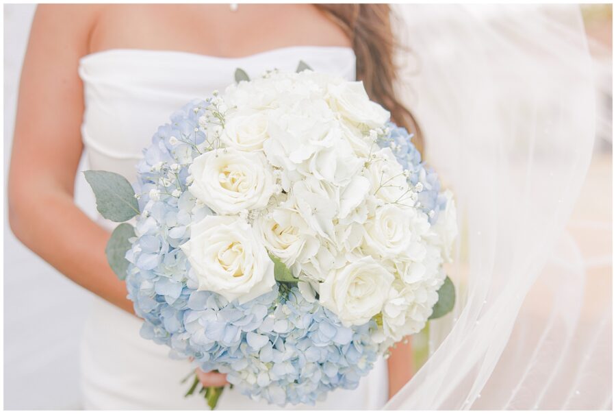 Close-up of the bride holding a bouquet of white roses and blue hydrangeas.