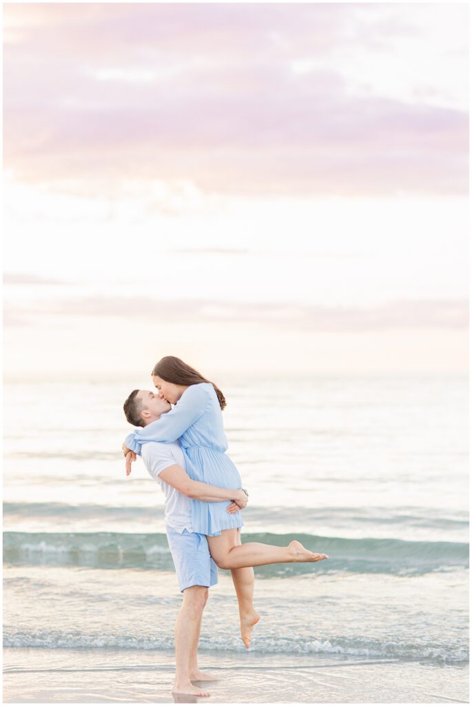 Man picking up and kissing woman by the ocean waves at Wingaersheek Beach