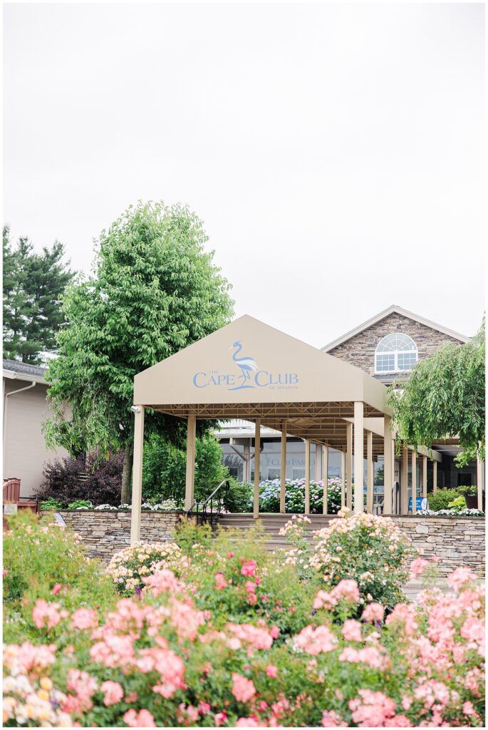 Entrance of the Cape Club of Sharon, surrounded by lush greenery and pink flowers.