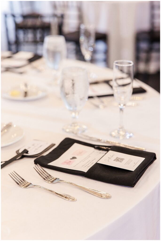 Close-up of a wedding table setting with utensils, glasses, and a black napkin with menus.