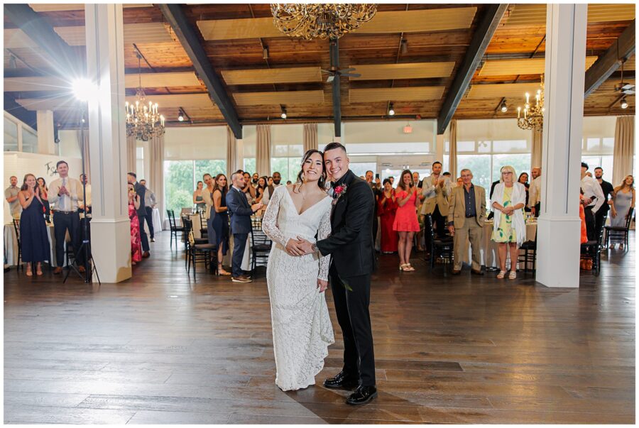 Bride and groom smiling while guests applaud.