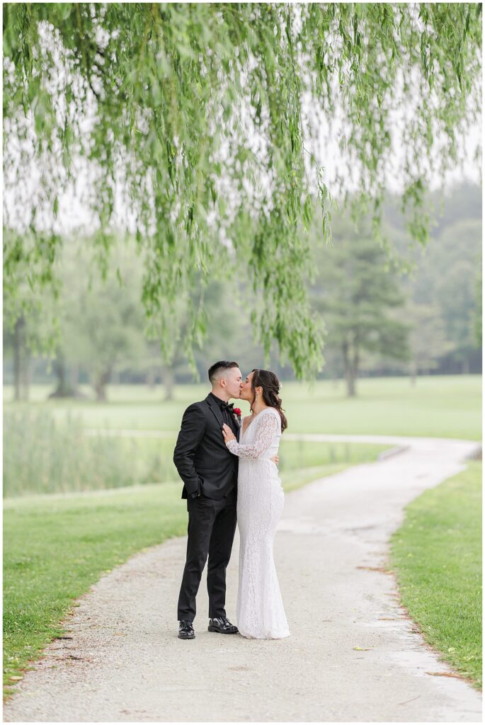 Bride and groom kissing under a weeping willow tree at the Cape Club of Sharon