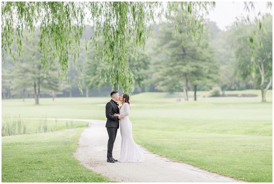 Bride and groom on a path under a willow tree at the Cape Club of Sharon