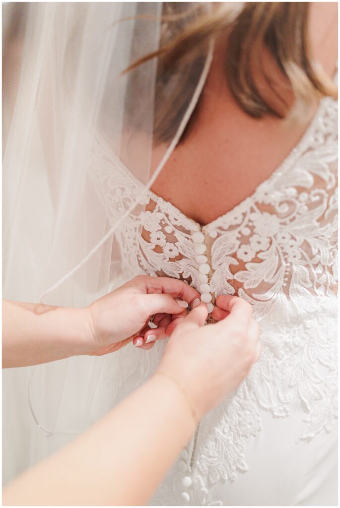 Close-up of hands buttoning lace wedding dress.