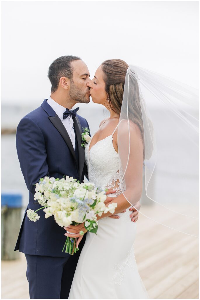 Bride and groom kissing, holding bouquet at Wychmere Beach Club.