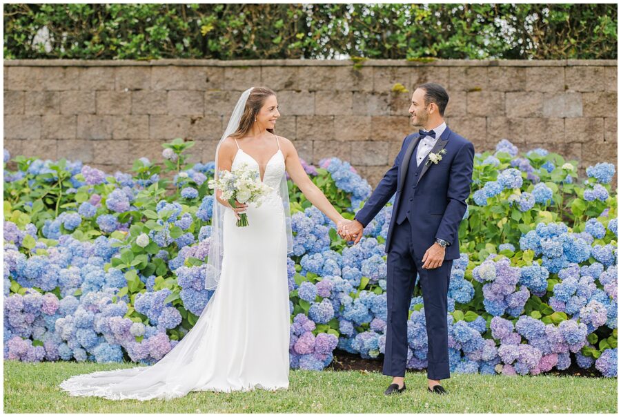 Bride and groom holding hands in front of hydrangeas at their wedding.