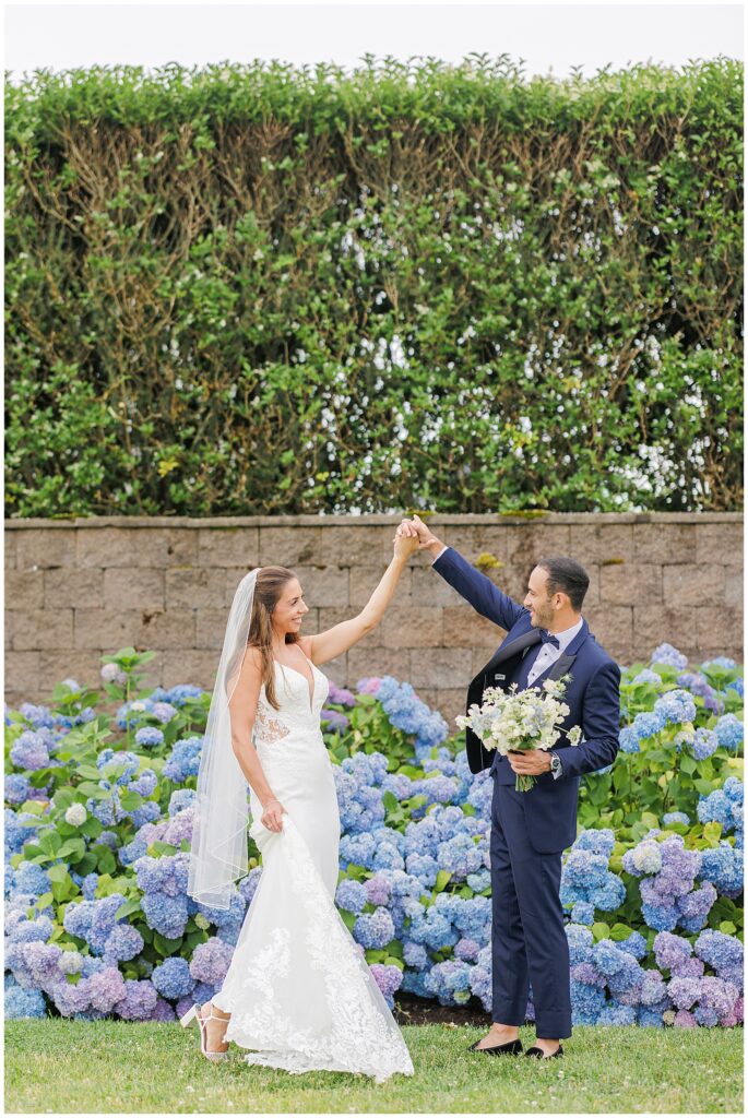 Groom twirling bride in front of a tall hedge at the Wychmere Beach Club.