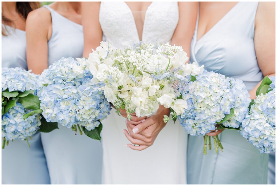 Close-up of bride and bridesmaids holding their bouquets of white and blue flowers.