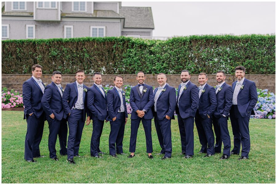 Groom with his groomsmen in blue suits standing in front of a hedge.