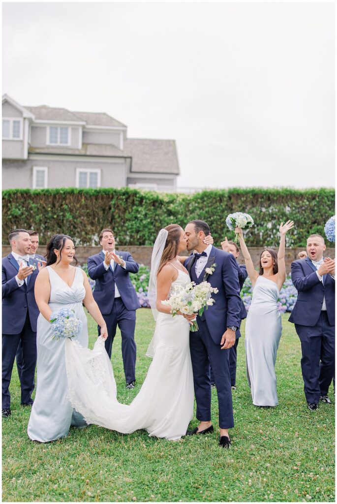 Bride and groom kissing while wedding party cheers behind them at the Wychmere Beach Club.