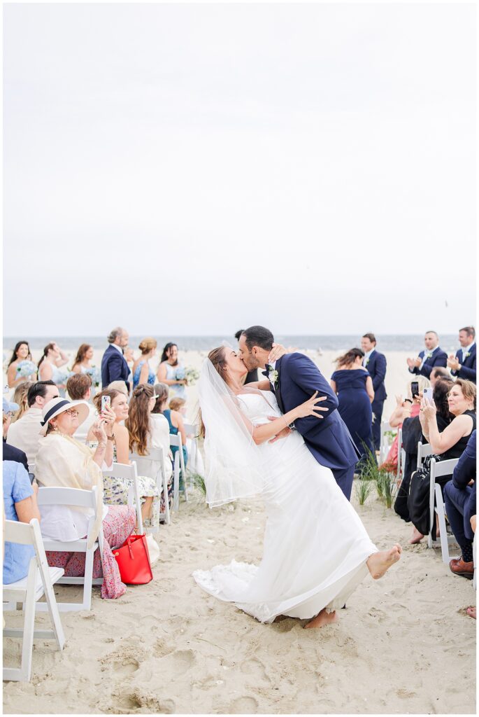 Bride and groom kiss in the aisle as guests cheer at Wychmere Beach Club.