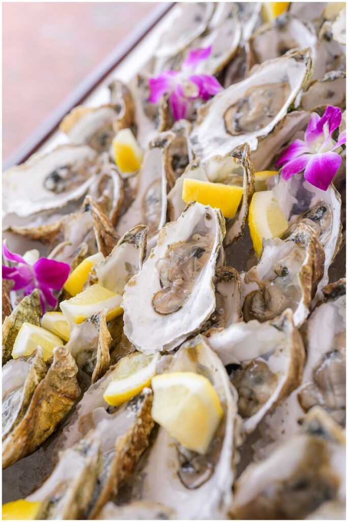 Close-up of oysters on the half shell garnished with lemon wedges and purple flowers.